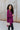 Side view of model wearing the This Is My Jam Sweater which features loose-knit magenta fabric with cuffed 3/4-length sleeves, a high-low hemline with side slits, and a rounded neckline.