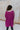 Back view of model wearing the This Is My Jam Sweater which features loose-knit magenta fabric with cuffed 3/4-length sleeves, a high-low hemline with side slits, and a rounded neckline.