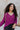 Front close up view of model wearing the This Is My Jam Sweater which features loose-knit magenta fabric with cuffed 3/4-length sleeves, a high-low hemline with side slits, and a rounded neckline. Sweater is tucked in the front. 