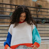 Close up view of model wearing the Don't Block My View Sweater which features ivory, orange, royal blue and aqua blue knit fabric, a round neckline, balloon sleeves with ribbed trim, and a cropped waist. Front of the sweater is tucked. 