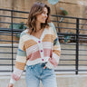 Front view of model wearing the Not Your Average Cardigan which features blue, sage, yellow, camel, light pink and mauve knit fabric with white trim, purple buttons on the front, a v-neckline and balloon long sleeves with ribbed wrists.