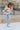 Side view of model wearing the Not Your Average Cardigan which features blue, sage, yellow, camel, light pink and mauve knit fabric with white trim, purple buttons on the front, a v-neckline and balloon long sleeves with ribbed wrists.