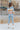 Full body back view of model wearing the Not Your Average Cardigan which features blue, sage, yellow, camel, light pink and mauve knit fabric with white trim, purple buttons on the front, a v-neckline and balloon long sleeves with ribbed wrists.