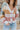 Close up view of model wearing the Not Your Average Cardigan which features blue, sage, yellow, camel, light pink and mauve knit fabric with white trim, purple buttons on the front, a v-neckline and balloon long sleeves with ribbed wrists.