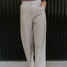 Front view of model wearing the You Should Be Dancing Pant which features taupe crinkle fabric, a zipper and hook closure, two front pockets and wide straight legs.