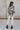 Full body back view of model wearing the Positive Vibes Top which features satin fabric with a cream and black geometric print, a button-up front with a collared neckline, and long sleeves with buttoned cuffs.