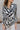 Close up view of model wearing the Positive Vibes Top which features satin fabric with a cream and black geometric print, a button-up front with a collared neckline, and long sleeves with buttoned cuffs.