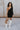 Full body view of model wearing the Shelby Color Block Dress which features black and brown color blocked ribbed fabric, one long sleeve and one adjustable spaghetti strap.