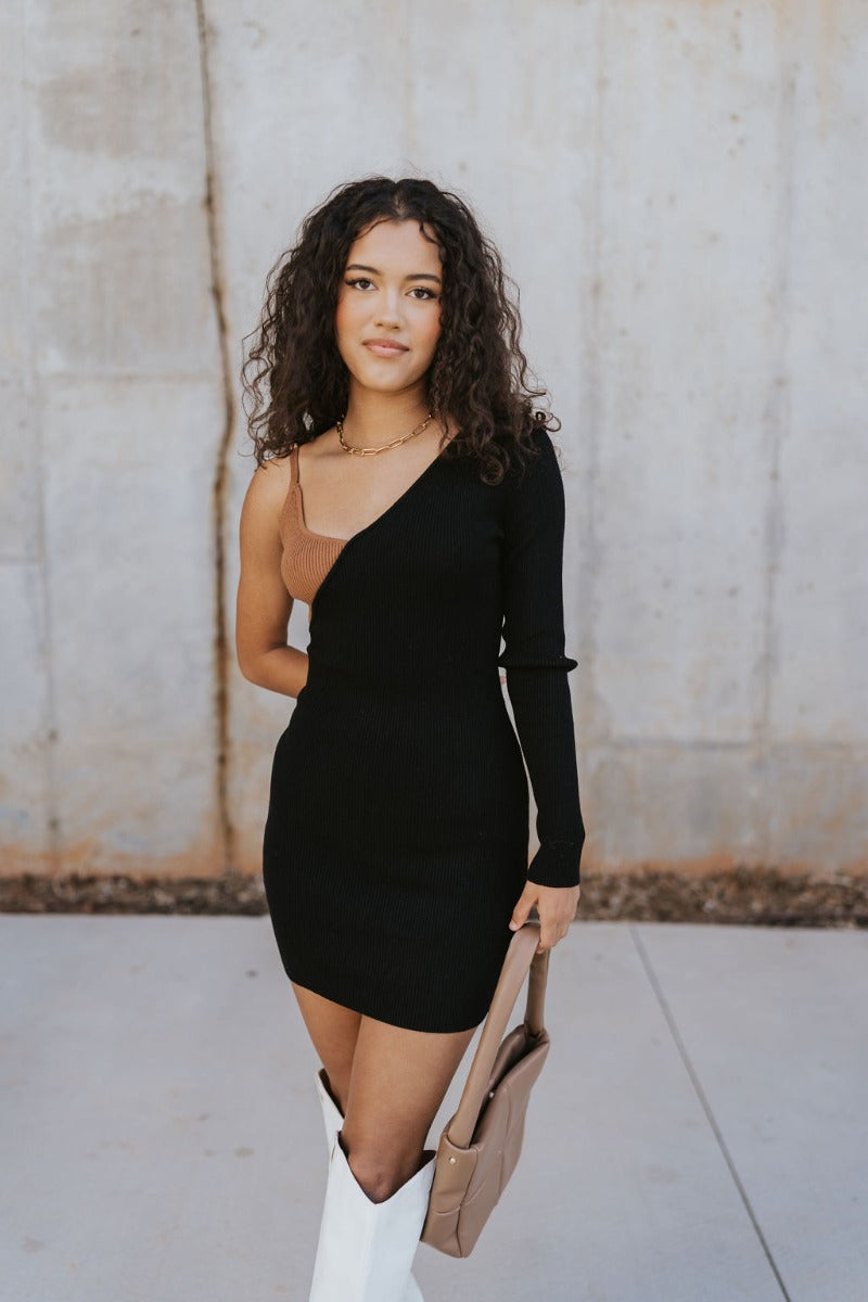 Close up view of model wearing the Shelby Color Block Dress which features black and brown color blocked ribbed fabric, one long sleeve and one adjustable spaghetti strap.