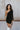 Close up view of model wearing the Shelby Color Block Dress which features black and brown color blocked ribbed fabric, one long sleeve and one adjustable spaghetti strap.