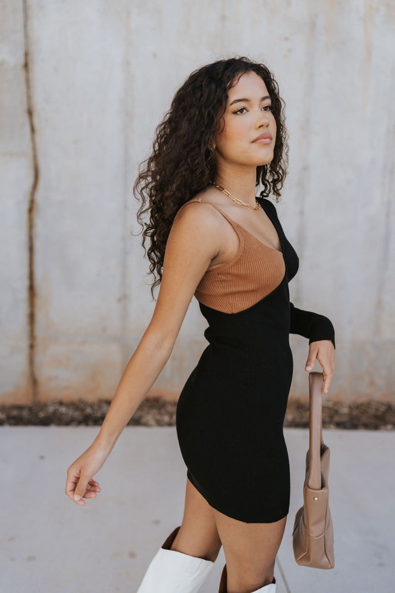 Right side view of model wearing the Shelby Color Block Dress which features black and brown color blocked ribbed fabric, one long sleeve and one adjustable spaghetti strap.