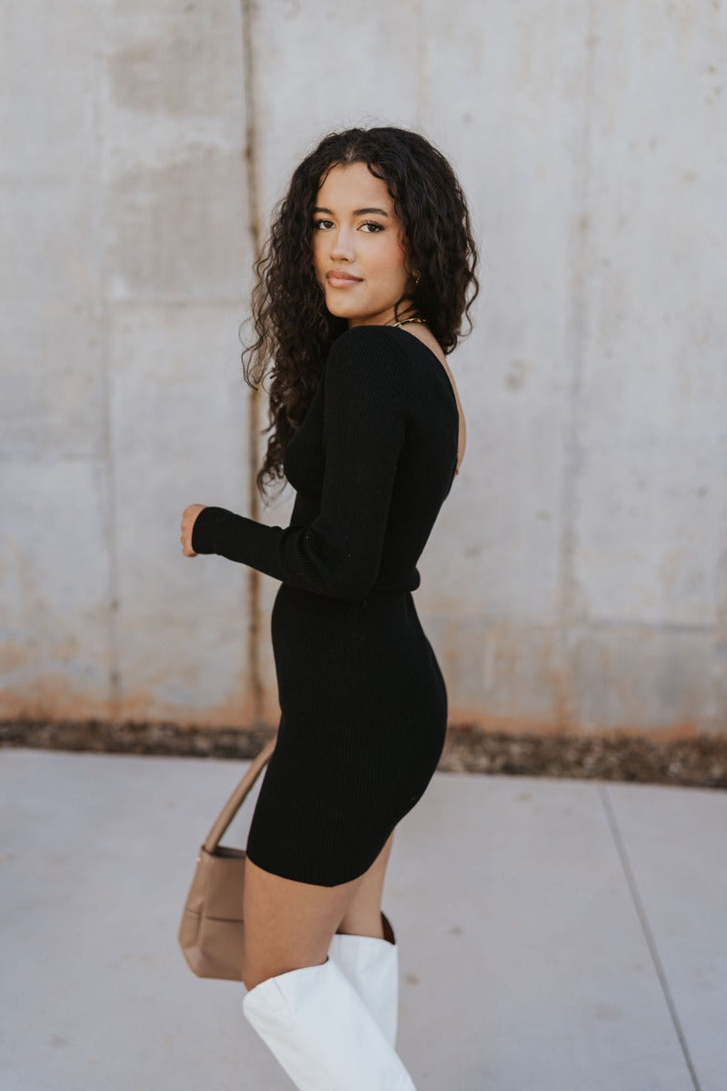 Left side view of model wearing the Shelby Color Block Dress which features black and brown color blocked ribbed fabric, one long sleeve and one adjustable spaghetti strap.