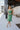 Full body view of model wearing the Feeling Lucky Midi Dress which features green fabric with a metallic sheen, a green lining, adjustable thin straps that tie across the back, and a side zipper.