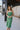 Close up view of model wearing the Feeling Lucky Midi Dress which features green fabric with a metallic sheen, a green lining, adjustable thin straps that tie across the back, and a side zipper.