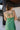 Close up back view of model wearing the Feeling Lucky Midi Dress which features green fabric with a metallic sheen, a green lining, adjustable thin straps that tie across the back, and a side zipper.