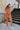 Full body back view of the Talk To Me Jumpsuit which features rust corduroy fabric, a front zipper with a silver button closure, 2 chest pockets, 2 side pockets, a collared neckline and short sleeves.