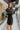 Side view of model wearing the Promise Me Dress, that has lined black fabric with a surplice neckline, a smocked waist, a tiered skirt, and semi-sheer long sleeves with a slight sheen and elastic wrists