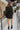 Full body view of model wearing the Promise Me Dress, that has lined black fabric with a surplice neckline, a smocked waist, a tiered skirt, and semi-sheer long sleeves with a slight sheen and elastic wrists