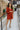Full body front view of model wearing the Falling Fast Dress, that has rust-colored fabric, a v-neckline, ruffle details on the shoulders, long balloon sleeves with elastic wrists, and side pockets
