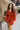 Front view of model wearing the Falling Fast Dress, that has rust-colored fabric, a v-neckline, ruffle details on the shoulders, long balloon sleeves with elastic wrists, and side pockets