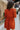 Bacl view of model wearing the Falling Fast Dress, that has rust-colored fabric, a v-neckline, ruffle details on the shoulders, long balloon sleeves with elastic wrists, and side pockets