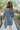 Back view of model wearing the Great Escape Denim Dress, that has washed black lightweight denim, a button-up front with silver buttons, a collared neckline, long sleeves with ruffled elastic wrists, and side pockets