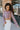 Side view of model wearing the So Over It Sweater, that has a beige, purple, blue, and olive digital striped pattern with orange lettuce trim, a cropped waist, long sleeves, and a round neckline.