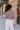 Back view of model wearing the So Over It Sweater, that has a beige, purple, blue, and olive digital striped pattern with orange lettuce trim, a cropped waist, long sleeves, and a round neckline.