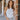 Front view of model wearing the Talia Bodysuit In White, that has white ribbed fabric, a round neckline, and a thong bottom with hook closures. Worn with jeans.