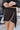 Close front view of model wearing the What A Night Fringe Skirt, that features black satin fabric with silver beaded fringe, a wrap waist with a side tie, and a back zipper.