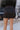 Close back  view of model wearing the What A Night Fringe Skirt, that features black satin fabric with silver beaded fringe, a wrap waist with a side tie, and a back zipper.