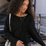 Front view of model wearing the Riley Waffle-Knit Top, which features black waffle knit fabric, raw hem details, scoop neckline, long sleeves with lettuce trim and drop shoulder.