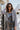 Front view of model wearing the All Or Nothing Cropped Blazer, that has brown and off white fabric with a plaid pattern, a cropped waist with a tortoise button closure, a collared neckline, and long sleeves.