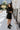Full body front view of model wearing the Elodie Dress in Black, which features black ribbed fabric, a high neck with lettuce trim, long sleeves, and a flared skirt