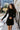 Front view of model wearing the Elodie Dress in Black, which features black ribbed fabric, a high neck with lettuce trim, long sleeves, and a flared skirt