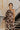 Front view of model wearing the Good Vibes Floral Top, that has brown light weight fabric with taupe flowers pattern, one shoulder with a long sleeve, a cropped waist, and a brown zipper on the left side. Tucked into matching pants.