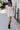 Full body front view of model wearing the Elodie Dress in Cream, which features cream ribbed fabric, a high neck with lettuce trim, long sleeves, and a flared skirt