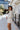 Side view of model wearing the Elodie Dress in Cream, which features cream ribbed fabric, a high neck with lettuce trim, long sleeves, and a flared skirt