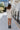 Full body back view of model wearing the Elodie Dress in Cream, which features cream ribbed fabric, a high neck with lettuce trim, long sleeves, and a flared skirt