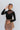Front view of model wearing the Last Call Bodysuit, which features black velvet with a mesh neckline, long sleeves, and a cheeky bottom. Worn with plaid skirt.