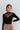 Front view of model wearing the Last Call Bodysuit, which features black velvet with a mesh neckline, long sleeves, and a cheeky bottom. Worn with plaid skirt.