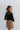 Back view of model wearing the Last Call Bodysuit, which features black velvet with a mesh neckline, long sleeves, and a cheeky bottom. Worn with plaid skirt.