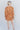 Full body back view of model wearing the Golden Hour Paisley Dress features camel-colored fabric with a paisley print, a surplice neckline, a tie belt and long sleeves with ruffled wrists