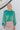Front view of model wearing the Lost In Your Eyes Top, which features a green satin fabric, long sleeves, a round high neckline with pleating, and an elastic waist.