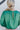 Close-up back view of model wearing the Lost In Your Eyes Top, which features a green satin fabric, long sleeves, a round high neckline with pleating, and an elastic waist.