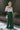 Full body front view of model wearing the Nothing But Love Pants, that have dark green fabric with inverted front pleating, an attached tie belt, wide flowy legs, and a side zipper. Worn with white top.