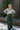 Full body front view of model wearing the Nothing But Love Pants, that have dark green fabric with inverted front pleating, an attached tie belt, wide flowy legs, and a side zipper. Worn with white top.