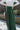 Front view of model wearing the Nothing But Love Pants, that have dark green fabric with inverted front pleating, an attached tie belt, wide flowy legs, and a side zipper. Worn with white top.