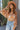 Front view of model wearing the Dream Girl Floral Bodysuit, that has camel and ivory floral print, a surplice neckline, flowy batwing sleeves, and a bikini bottom with a snap closure. Worn with jeans.