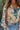 Close front view of model wearing the First Love Floral Top, that has teal fabric with a metallic gold and ivory floral print, a surplice neckline, flowy balloon sleeves with smocked cuffs, and an elastic waist